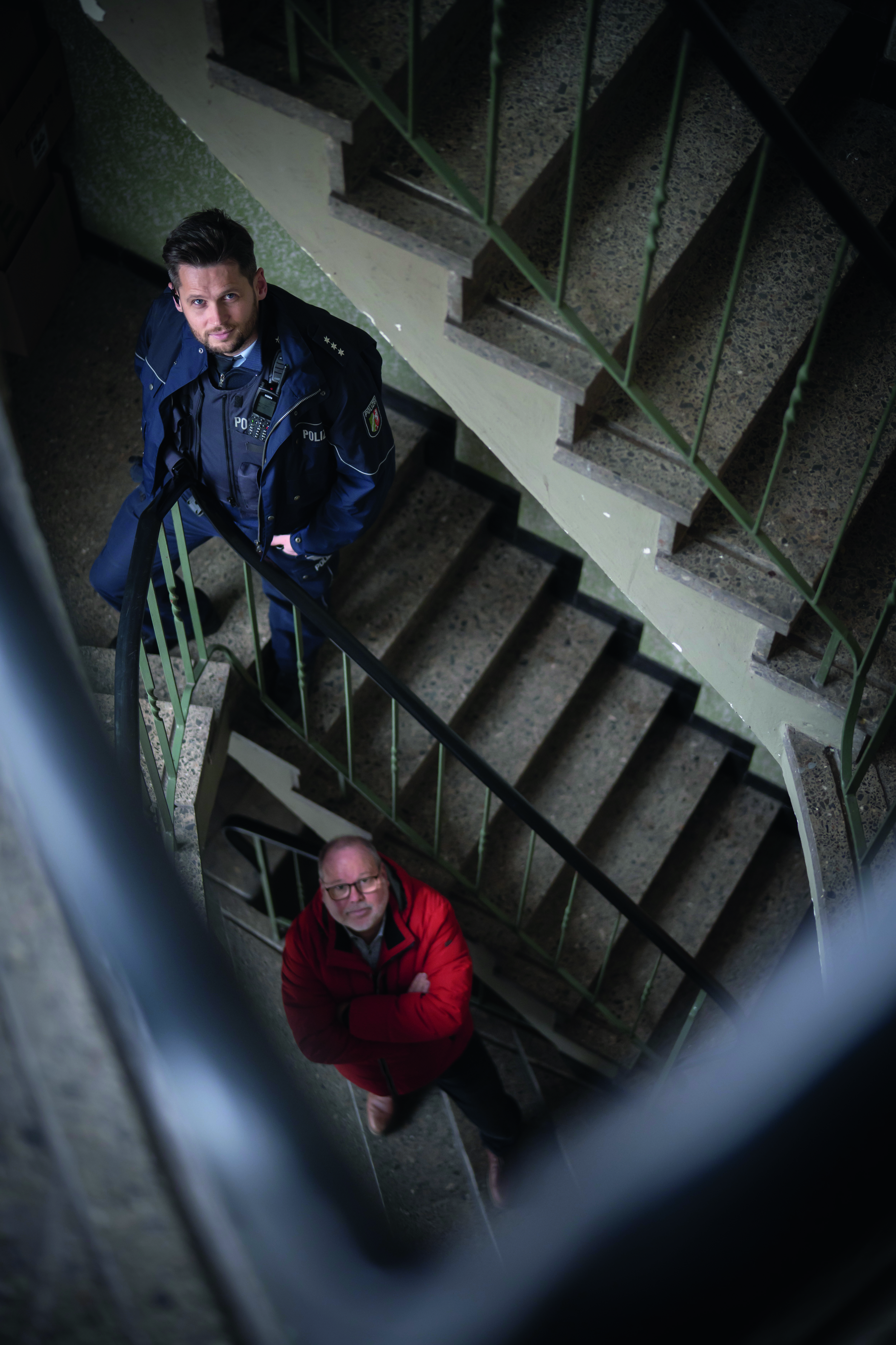 Polizeihauptkommissar Lukas Serafin und Jörg Lange, Leiter der Stabsstelle Sozialleistungsbetrug bei der Stadt Duisburg stehen im Treppenhaus eines Mehrfamilienhauses und blicken nach oben in die Kamer 