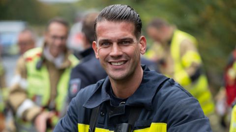Christoph Pütz, operational trainer of the Aachen fire brigade can be seen in the Forntal funding ground. He smiles into the camera. He is on a highway during an operational exercise.In the background,other firefighters can be seen.